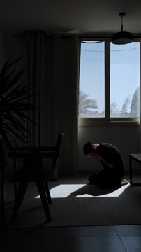 Man silhouette sitting on floor with face in hands during emotional breakdown, overwhelmed by despair and unable to cope alone at home, vertical video