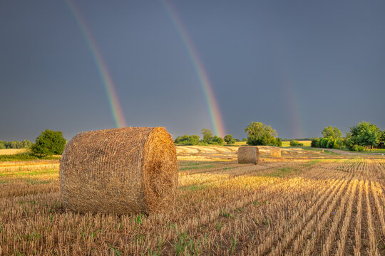 Twilight rainbow over a rain-washed field with hay bales.