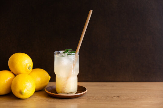 Citronnade glac&eacute;e avec paille naturelle, feuilles de menthe et citrons frais sur table en bois, fond sombre, espace de copie