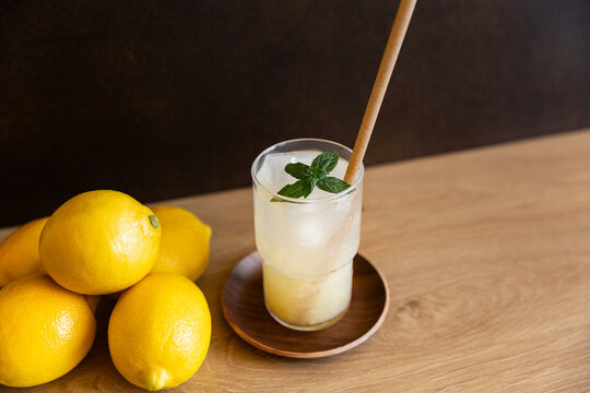 Citronnade glac&eacute;e servie dans un verre transparent avec une paille et des feuilles de menthe, table en bois, fond brun, citrons jaunes pos&eacute;s &agrave; gauche du verre, vue en plong&eacute;e, sensation de fra&icirc;cheur 