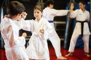 Boy and girl in kimonos train karate techniques in group in studio © JackF