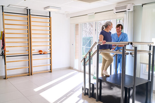 Senior Woman Doing Stair Climbing Exercise With Physiotherapist Assistance In Rehab Center For Injury Recovery And Rehabilitation Program Indoors