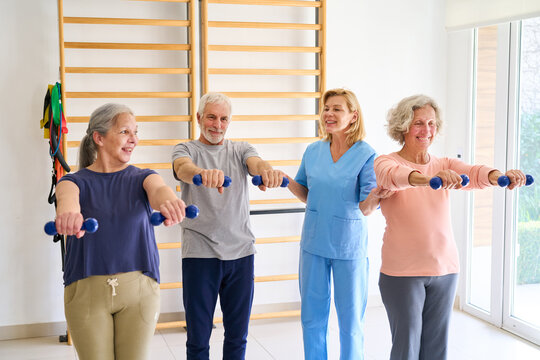 Senior Adults Doing Dumbbell Exercises With Physiotherapist In Rehab Center For Strength And Mobility Training Indoor Rehabilitation Program