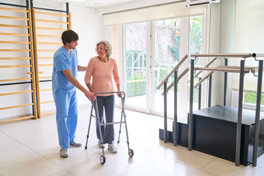 Senior Woman Using Walker With Physiotherapist Assistance In Rehab Center For Recovery And Rehabilitation After Injury Indoors