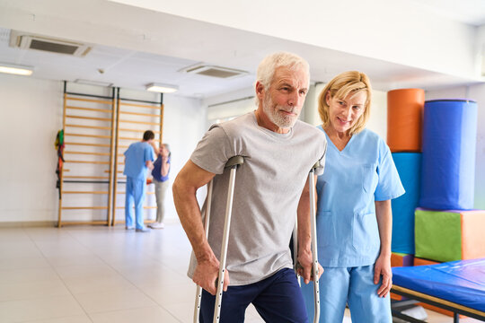 Senior Man Using Crutches Assisted By Physiotherapist In Rehab Center For Mobility Training And Injury Recovery Indoor Physical Therapy Session
