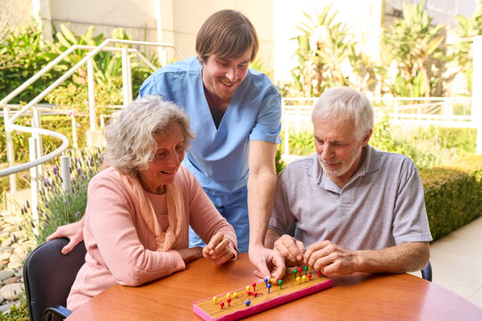 Senior Couple Playing Game With Physiotherapist Outdoors At Rehab Center For Cognitive Therapy And Rehabilitation After Injury Or Stroke Recovery