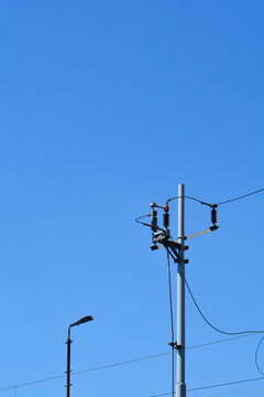 An outdoor shot of a grey metal utility pole with electrical components and power lines under a clear blue sky.