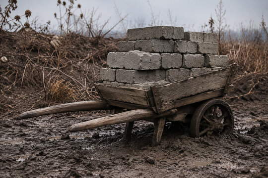 Old wooden wheelbarrow with concrete blocks in mud, heavy load and labor concept