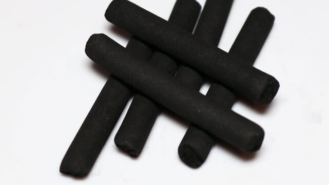A pile of black crayon sticks on a white surface. Rotating in a circle