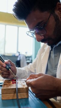 Vertical video of young adult Indian male engineer soldering microchip in robotics laboratory. Footage is suitable for tech education ads or hardware engineering school promos