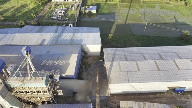 Aerial footage showing a factory smokestack releasing dense dark smoke over rural farmland, homes and green agricultural fields in Bangladesh, illustrating industrial air pollution and environmental
