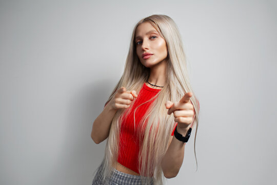 Pretty blond girl point index fingers on you, wearing red shirt isolated on grey background.