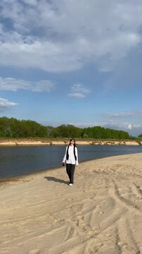 A woman is walking alone along a sandy riverbank in the summer. Relaxing in the summer atmosphere, and outdoor recreation, hiking