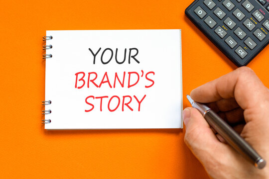 Branding and your brands story symbol. Concept words Your brands story on beautiful white note. Beautiful orange background. Businessman hand. Business branding your brands story concept. Copy space.