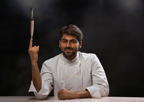 A CHEF SITTING IN FRONT OF CAMERA WHILE BALANCING KNIFE IN HANDS