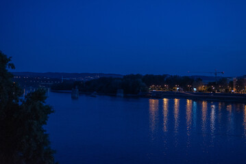Fototapeta premium Wide night view of calm river reflecting golden Novi Sad city lights under deep blue twilight sky