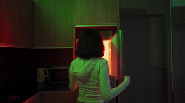 Young Woman Opening Refrigerator at Night for Late Midnight Snack in Atmospheric Dark Kitchen