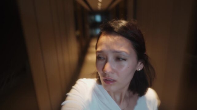 Asian woman walking along hallway covering face from flashing bright lights motion blur disoriented footage