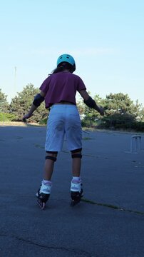 Girl in safety gear inline skating away across empty park asphalt