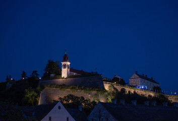 Illuminated Petrovaradin Fortress clock tower stands atop stone defensive walls at night in Novi Sad, Serbia © Denis Renkas