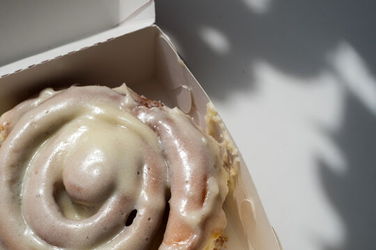 Fresh cinnamon roll with cream cheese frosting in takeaway cardboard box for bakery and dessert concept