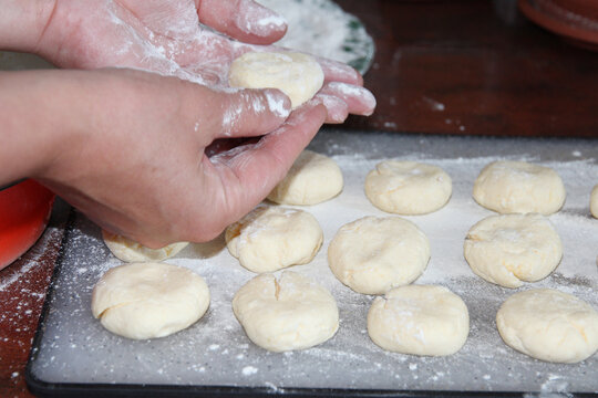 A close-up of a woman's hands forming homemade syrniki, cheesecakes over a floured surface. The process of preparing raw syrniki dough, ready to be shaped and baked