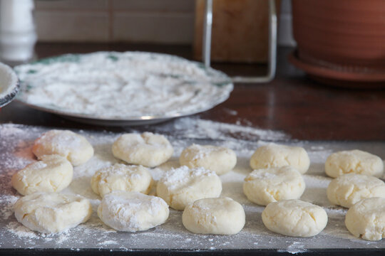 Close up Homemade cottage cheese pancakes, syrniki on a floured surface, with raw syrniki dough portions ready for shaping and cooking. Selective focus