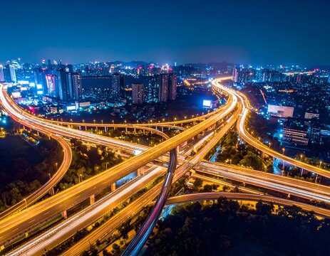 Aerial view of an illuminated highway interchange at night, with city skyline