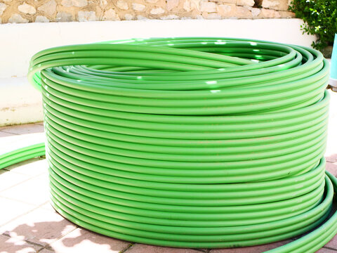 Large industrial roll of green plastic HDPE conduit pipe on pavement