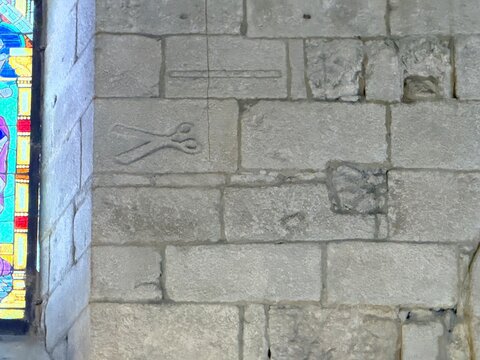 Muro de piedra antiguo con relieve de tijeras junto a una vidriera de colores en una Iglesia, A Coru&ntilde;a
