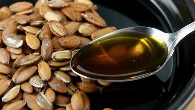 t42573 mp4 Culinary 4K Ultra HD video showing dark green pumpkin seed oil pouring smoothly from a metal spoon alongside shelled raw pumpkin seeds showcasing healthy plant oils vegan nutrition and