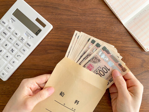 木製テーブルで給料袋からお金を取り出す女性の手