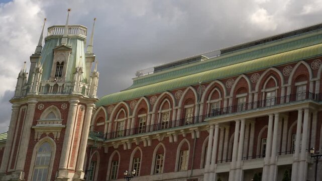 Historic palace towers and arcaded colonnade under partly cloudy sky with visiting crowd in foreground, with architecture, tower, turret, cupola detail, showing spire, pinnacle, copper, patina context