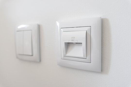 close up of modern white wall charger socket with usb ports and light switch at background