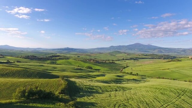 Aerial view of rolling green hills of the Tuscan countryside under a clear blue sky in Tuscany, Italy.