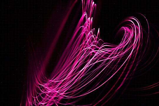 Pink light trails create abstract flowing patterns on a dark