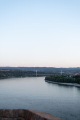 Obraz premium Wide Danube river flows through hilly landscape with bridge spanning across in the distance. Novi Sad, Serbia