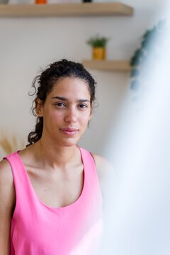 Young Hispanic woman with curly hair wears pink sleeveless top indoors