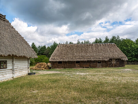 Thatched Barn And Rustic Farmhouses In Rural Countryside With Haystack And Wooden Outbuildings
