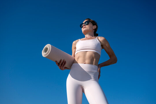 Fit woman in sportswear holding a rolled exercise mat outdoors,