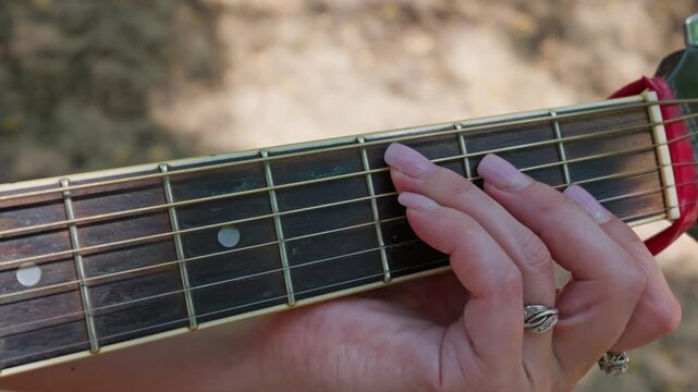 A woman hand presses strings on an acoustic guitar fretboard during a practice lesson. Concept of online music education, mastering chords, instrumental skill, and audio tutorial.