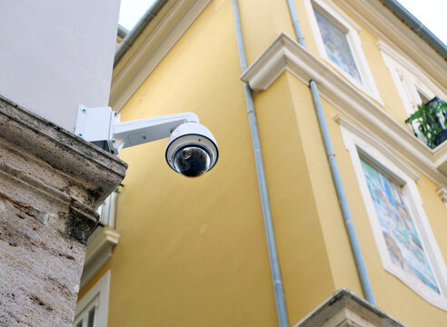 White modern cctv security camera mounted on stone wall of historical yellow building. Great concept for urban surveillance article, public safety presentation or property protection system banner