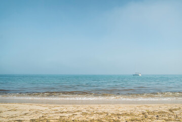 Small sailboat on the ocean horizon seen from a sandy beach, Tavira, Portugal © Elsworth Frobisher