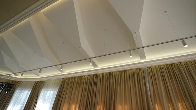 Vaulted ceiling with track spotlights and warm cove lighting over draped event stage, with ceiling, vaulted, soffit, cove detail, showing lighting, spotlight, track, fixture context