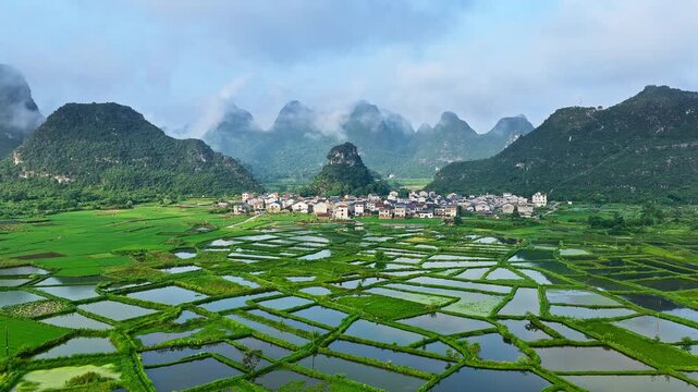 Aerial drone view of a traditional rural village surrounded by green rice fields and karst mountains in Guilin, China, showcasing the glass fields landscape in summer.