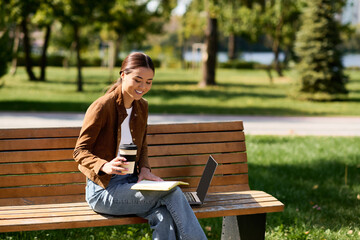 Fototapeta premium A young beautiful Asian woman leisurely sips coffee, absorbed in her work at a sunny park.