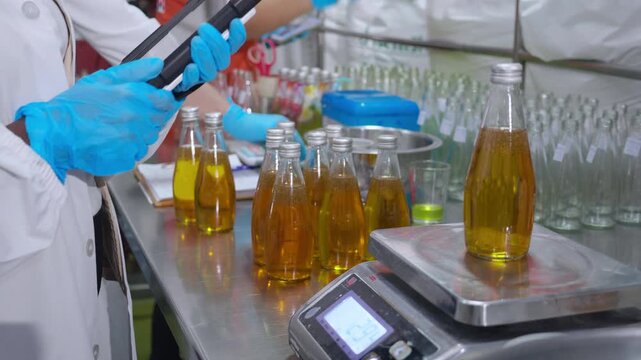 Woman engineer place fruit juice bottle on digital laboratory scale while recording precise weight data on tablet in beverage factory, food production industry, inspection process industrial.