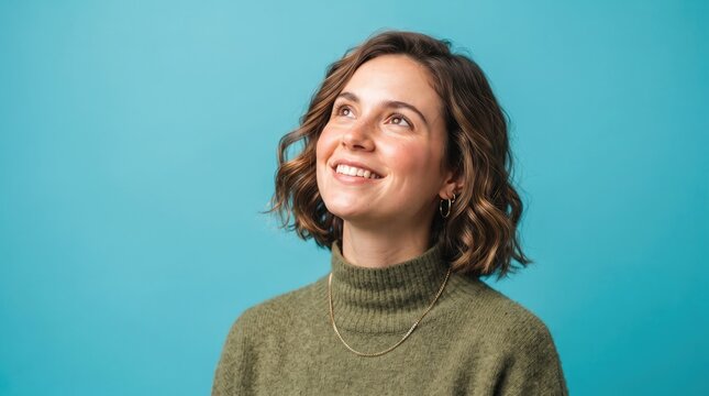 Beautiful young woman looking upwards with a gentle smile against a blue background