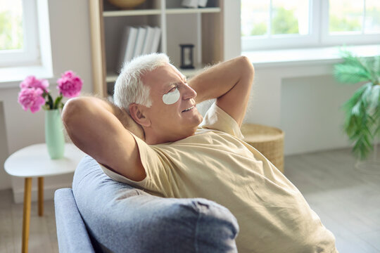 Senior man with skincare patches enjoying relaxation. Happy retiree enjoys retirement on a cozy home sofa after self care, embracing beauty and wellness. Concept of calm aging and wellness.