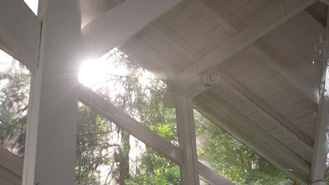 Sunlight streaming through triangular clerestory windows over white painted timber beams with visible lens flare and hazy rays, with sunlight, flare, glare, haze detail